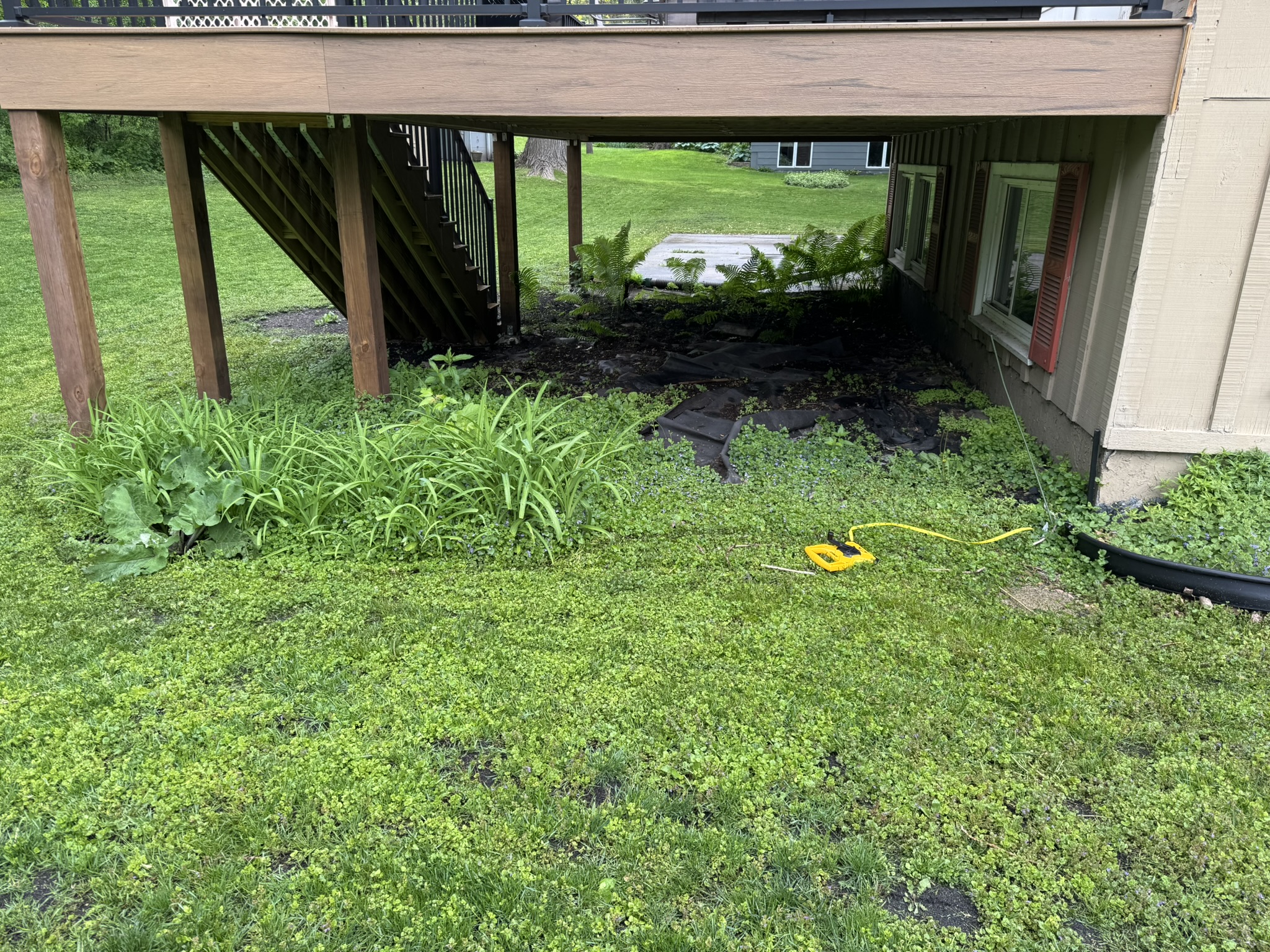 Backyard under a raised deck overgrown with weeds before a rock installation in Minnetonka Minnesota