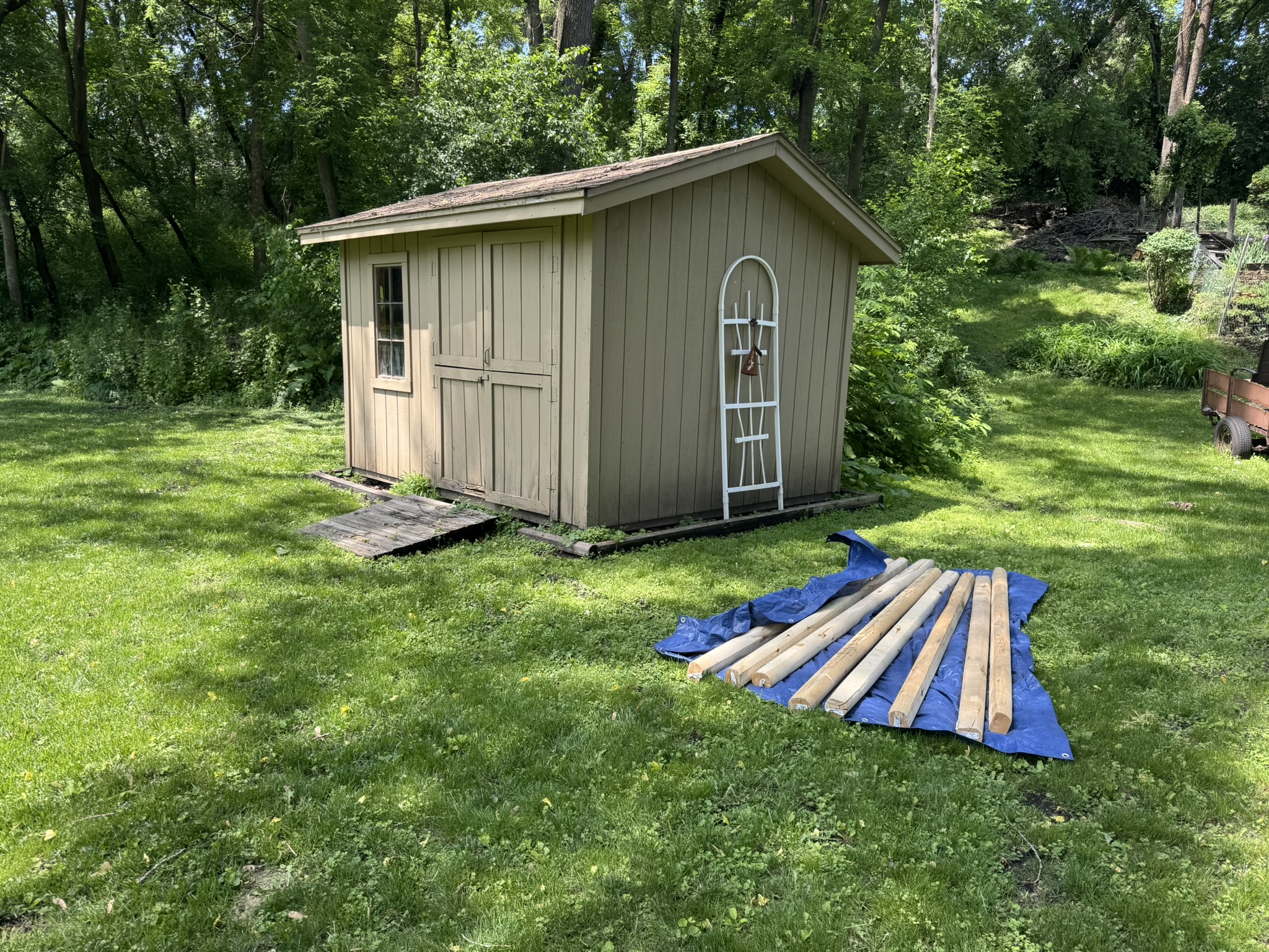 Storage shed on its old sagging base with new frame timbers staged on a tarp in Minnetonka Minnesota