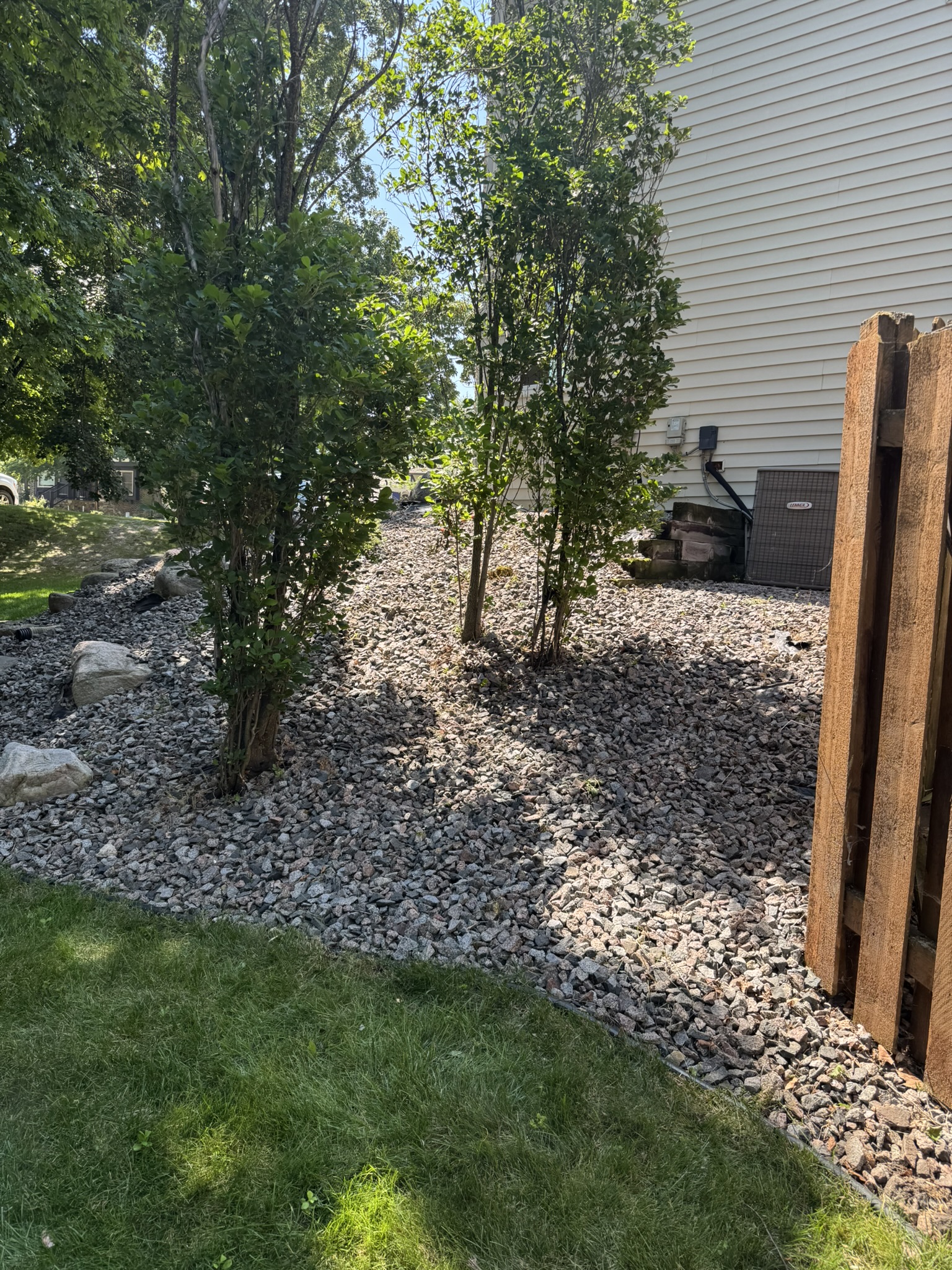Rock beds along the side of a house cleared of debris with shrubs and trees