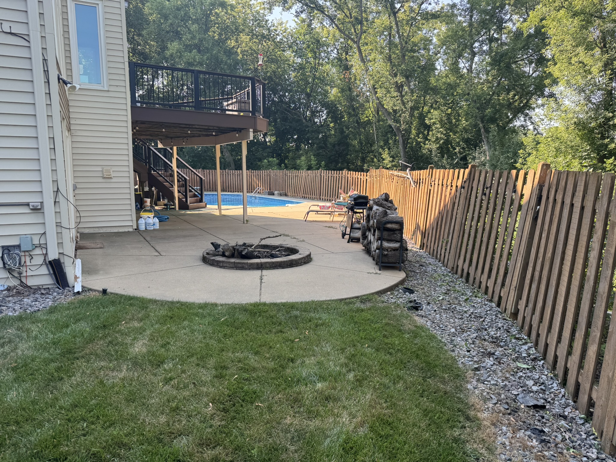 Backyard patio and fire pit with a mowed lawn and tidy rock border along the fence
